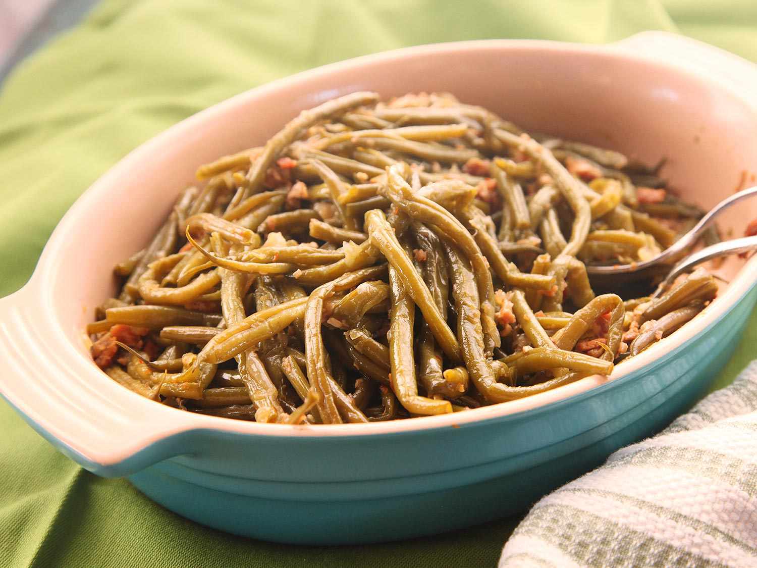 Bacon-Braised Green Beans in a blue Le Cruset serving dish on a green towel.