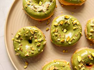 Doughnuts with pistachio cream and pistachios on top on a tan plate.