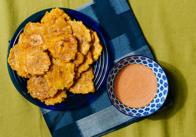 Overhead view of tostones on a blue plate with a blue napkin and bowl of dipping sauce