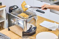 A person lifts fried food from the All-Clad Easy Clean Pro 3.5L Electric Deep Fryer with tongs