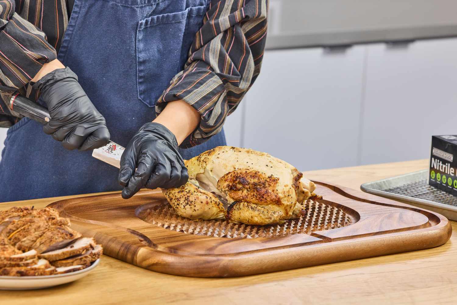 Person carving a roasted chicken on a Lipper International Acacia Cutting Board with Grid Grip