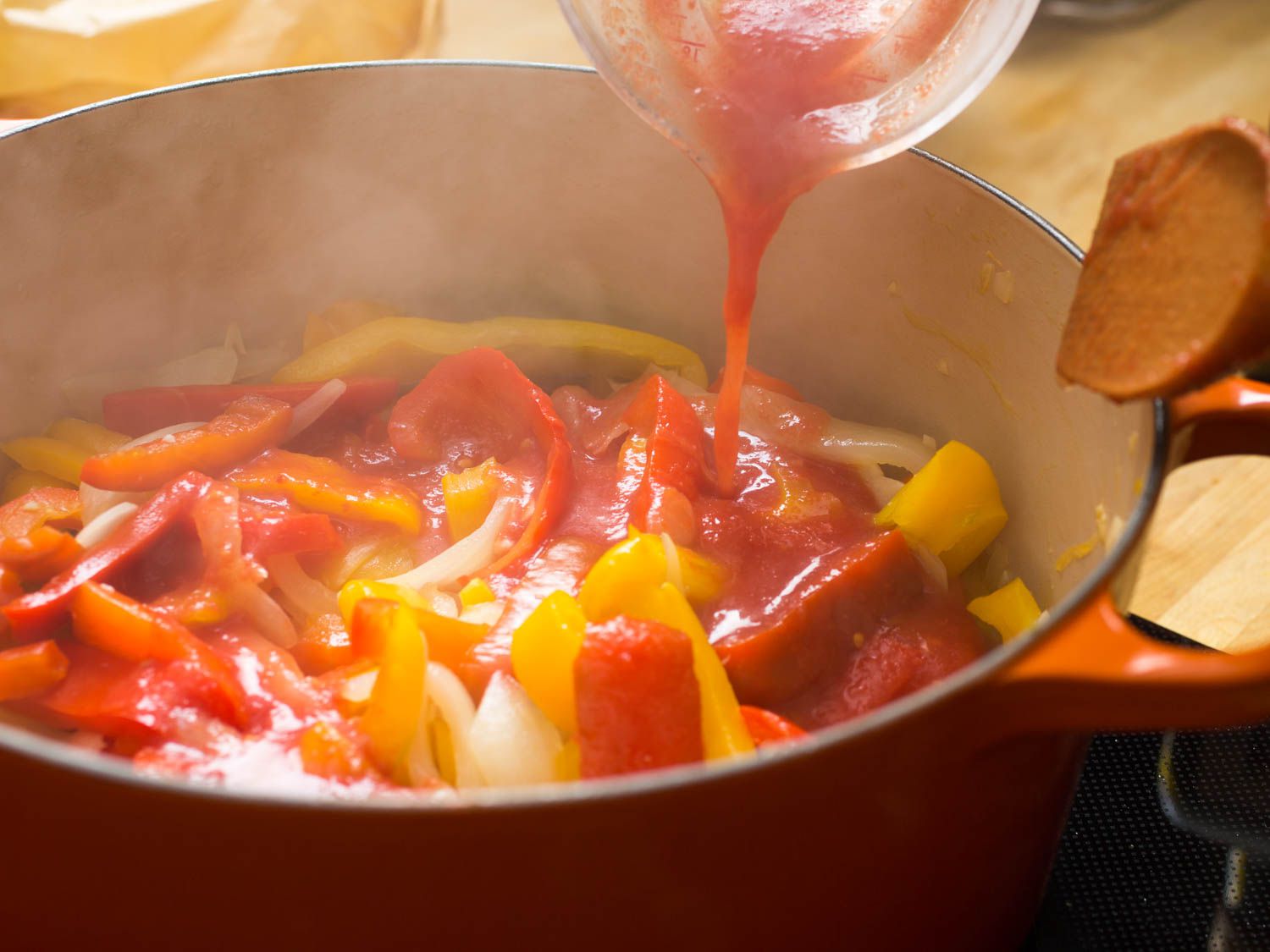 Pouring puréed tomatoes into bell peppers in a Dutch oven.