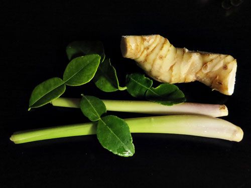 Makrut lime leaves, galangal, and lemongrass on a black background.