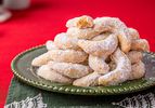 A stack of crescentshaped cookies dusted with powdered sugar arranged on a green plate placed over a festive napkin