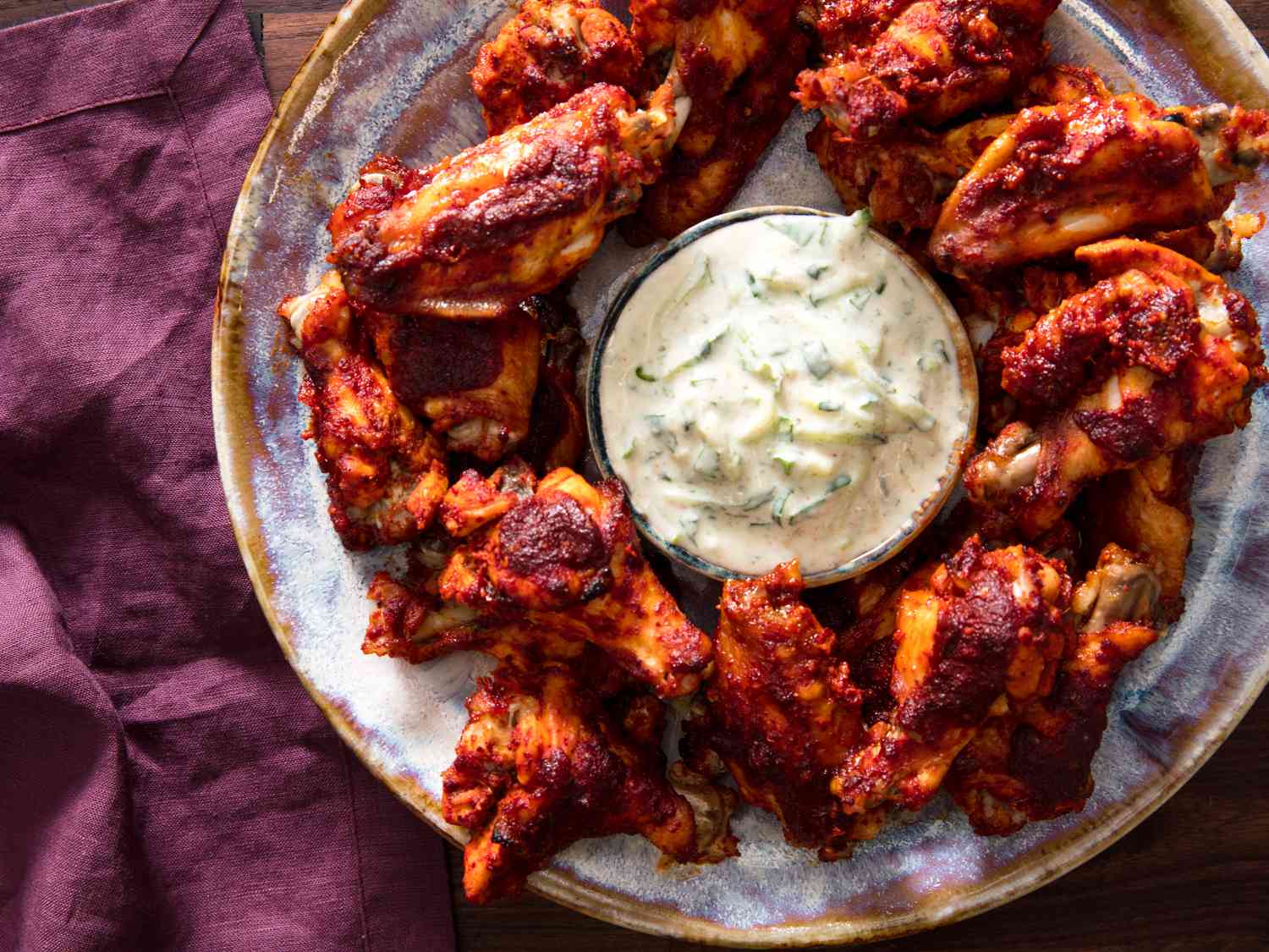 An overhead shot of a round plate holding tamarind-ginger glazed chicken wings. In the center of the plate is a small bowl of dipping sauce.