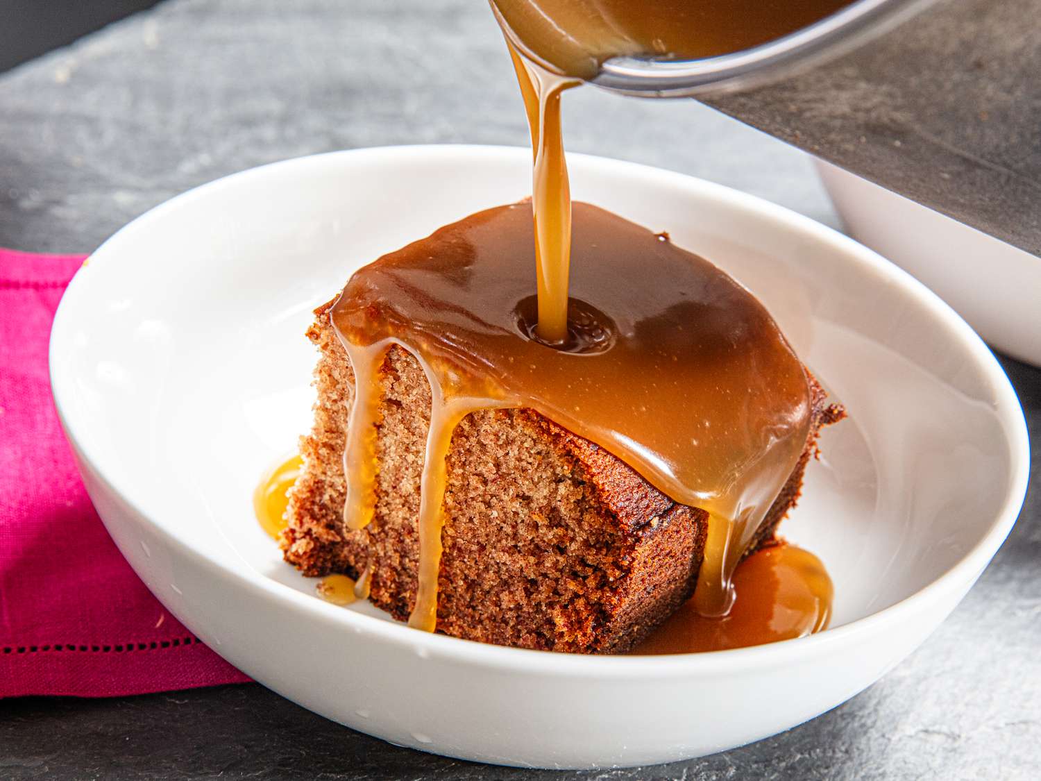 Side view of pouring caramel on sticky toffee pudding