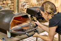 A person checks the temperature of the inside of the Ooni Karu 2 Pro Multi-Fuel Pizza Oven
