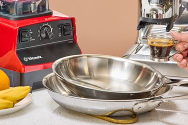 Kitchen appliances and utensils including a blender, frying pans, and an espresso machine with a cup of coffee being held