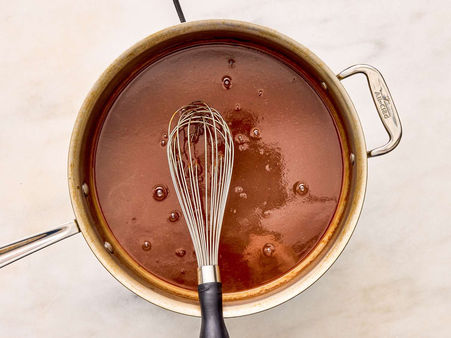 A saucepan with sauce being whisked on a kitchen counter