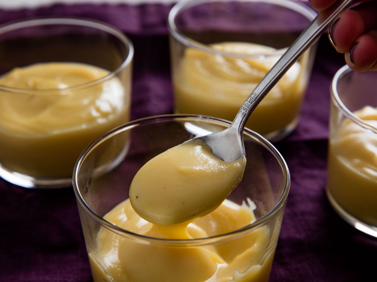 Four servings of butterscotch pudding. A spoonful of butterscotch pudding is held up to the camera.