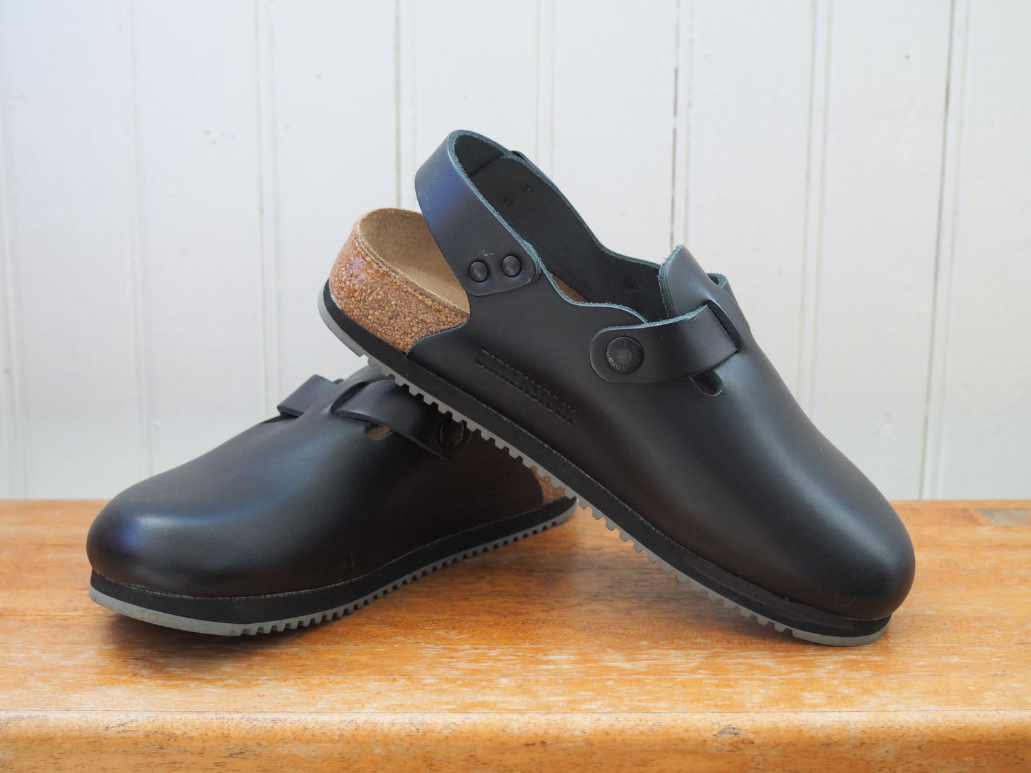 Black Birkenstock clogs on a wooden countertop.