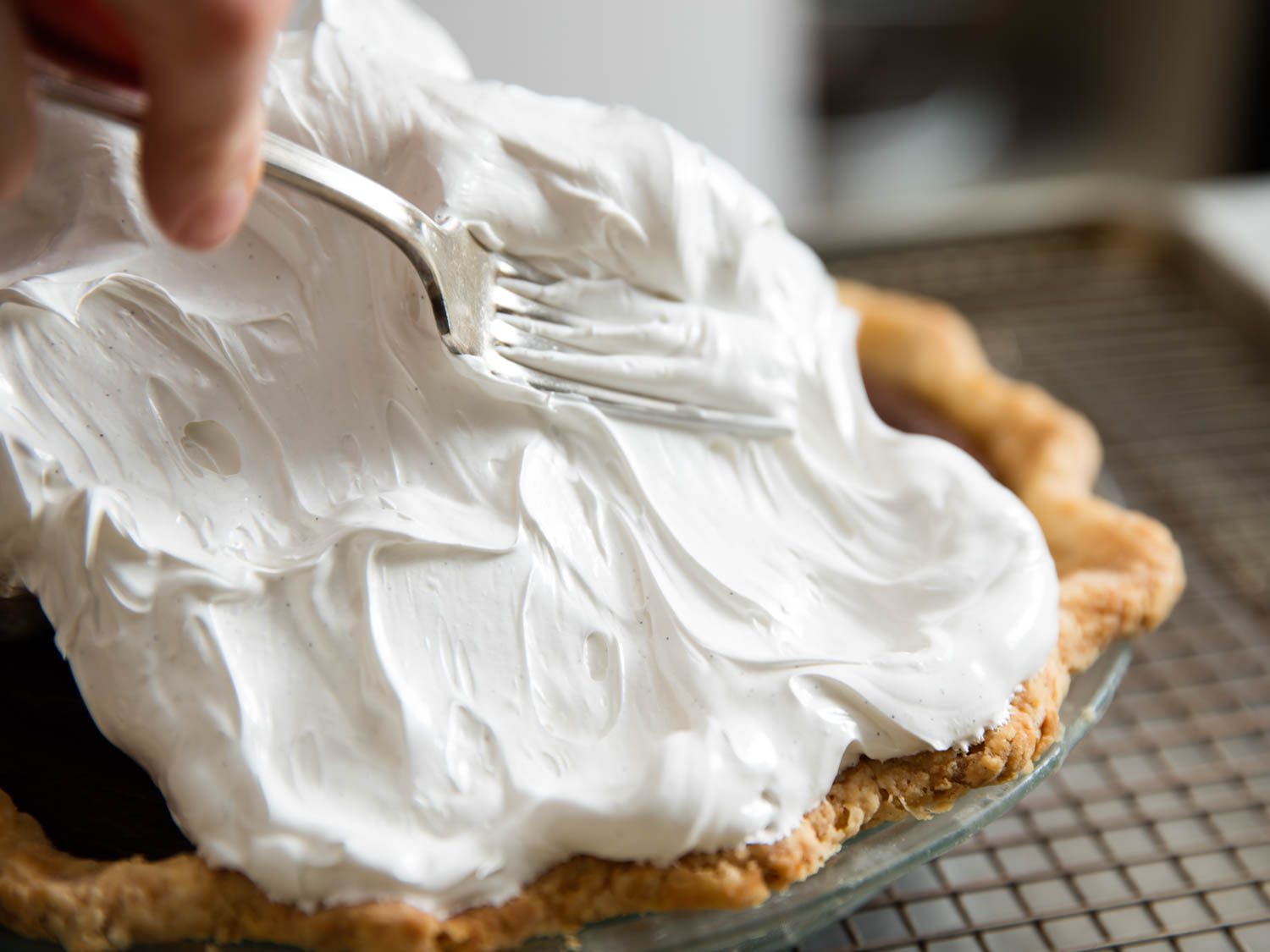 Close-up of author spreading Swiss meringue on top of pie with a fork.