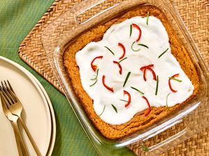 Overhead angle of whole squash souffle in glass baking dish, on a green fabric and woven placemat. Plate and forks on the side 