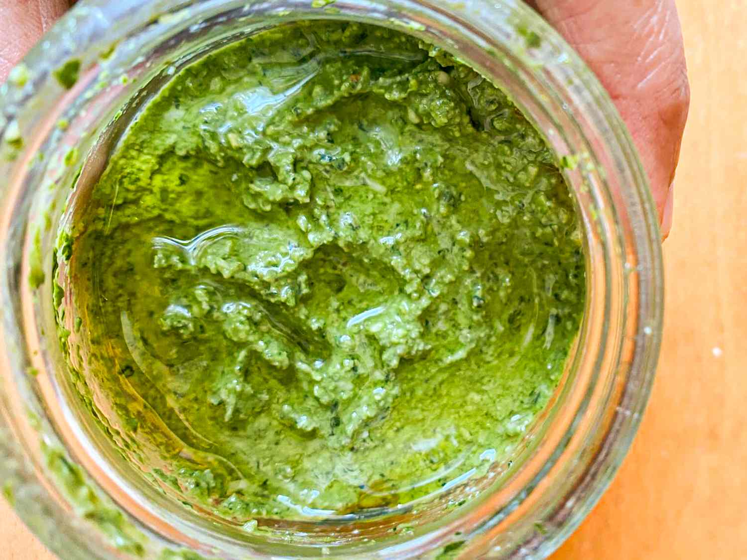 Jar of homemade pesto viewed from above featuring visible texture and green ingredients