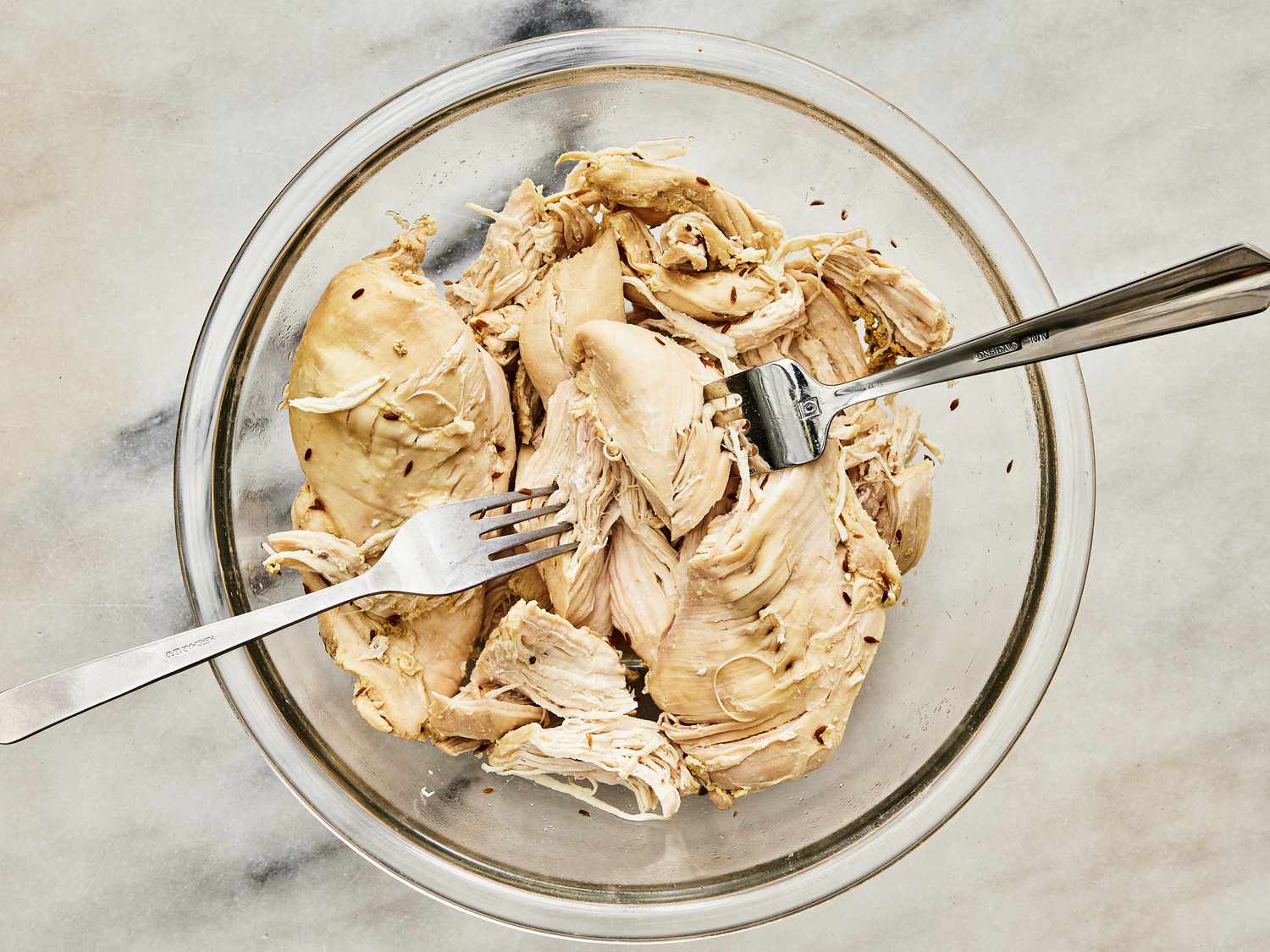 poached chicken in a glass bowl, shredded with 2 forks 