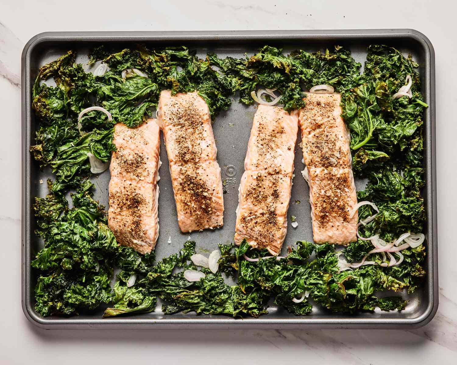 Four seasoned salmon fillets baked on a sheet pan with kale and onion slices
