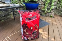 A bag of Jealous Devil brand charcoal placed outdoors next to a grill on a patio deck