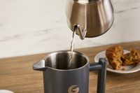 A person pouring water from a gooseneck kettle into the coffee gator French press.