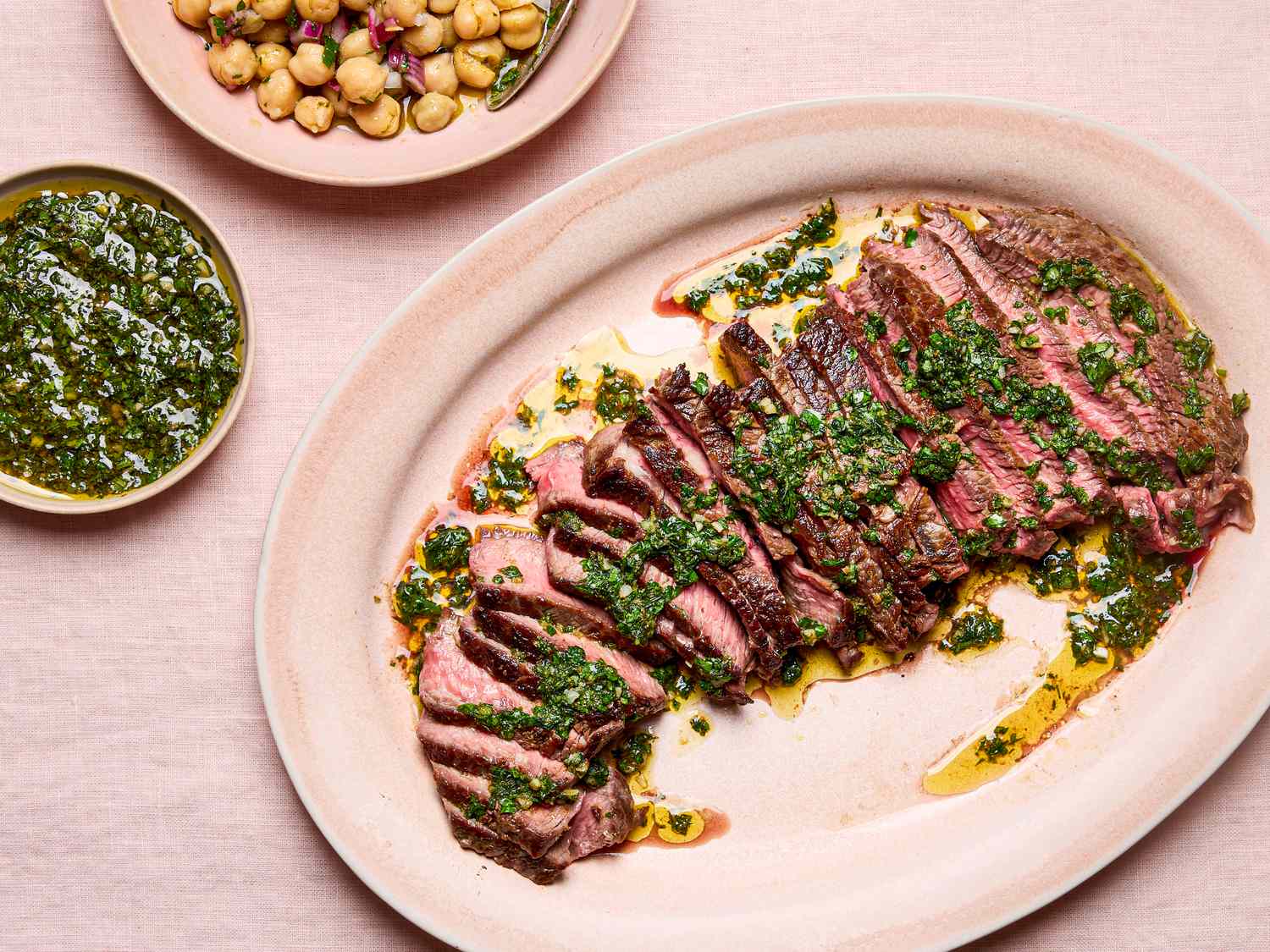Sliced steak with green chermoula garnished accompanied by a chickpea salad and a side of green sauce