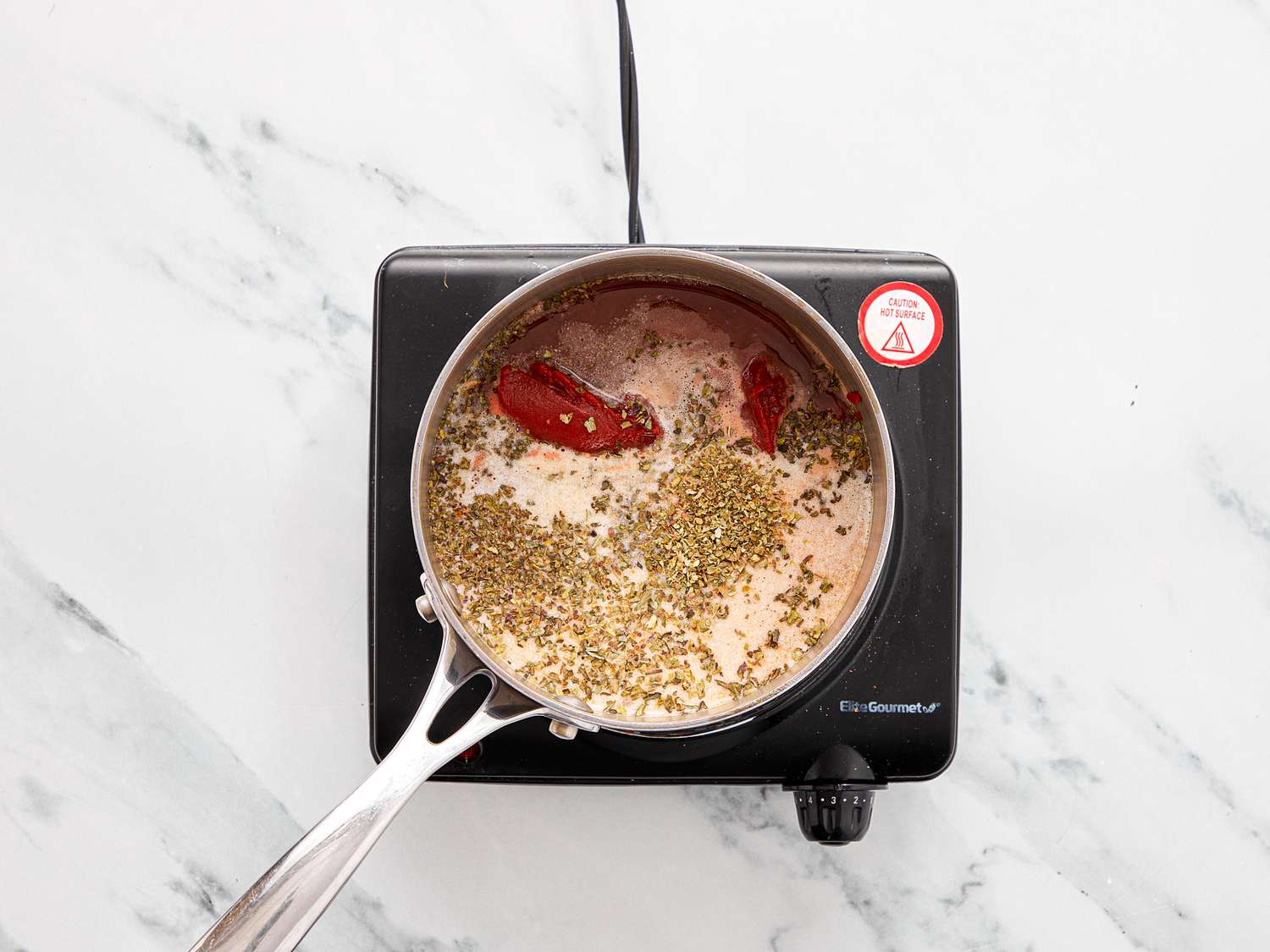 A saucepan with ingredients such as spices and liquids heating on a small portable stovetop