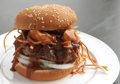 Profile view of a poutine burger, dripping with gravy, served on a white plate.