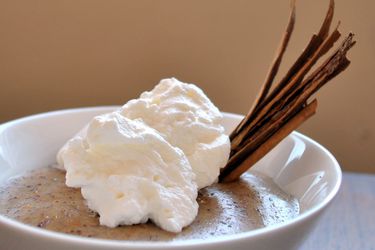 Closeup of cinnamon-orange pudding, served in a small white bowl with a slivered canela cinnamon garnish and whipped cream.