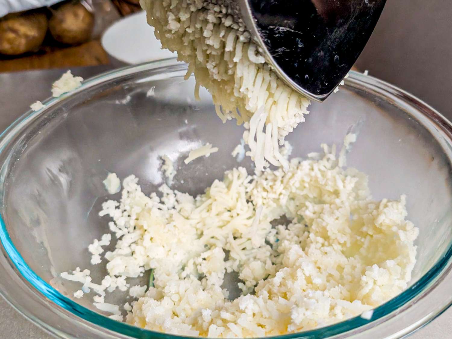 Potatoes being pressed into a bowl with a food ricer preparation for mashed potatoes