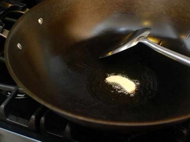 Infusing hot oil with slice of ginger in wok