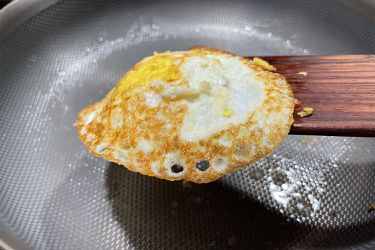 A cooked egg on a wooden spatula above a textured pan