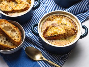 Overhead view of two bowls of french onion soup in small bowls on a striped blue background