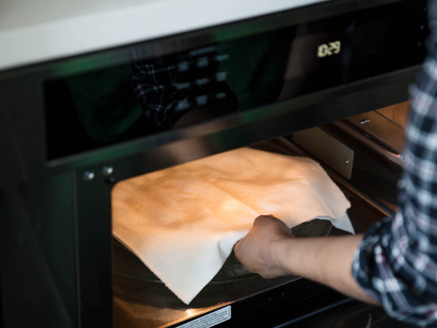 A hand pulling a covered tray out of the microwave