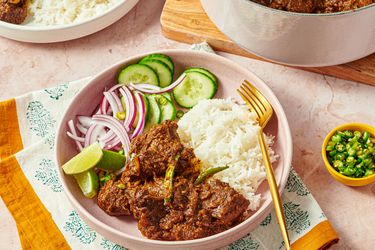 A plate with rice beef curry cucumber slices lime wedge and red onions served with a fork