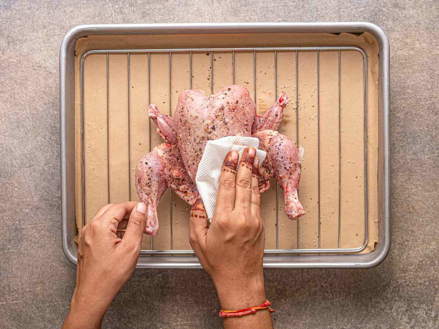 Person preparing a seasoned chicken on a baking rack