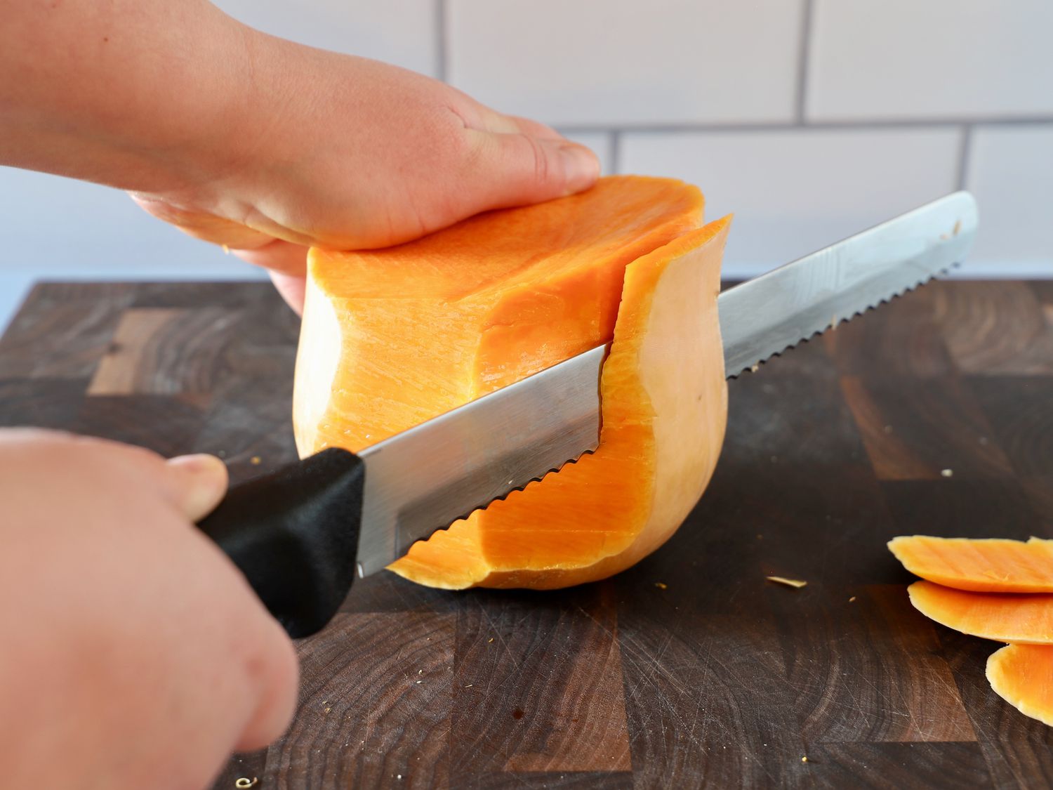 A person using a serrated bread knife to peel butternut squash.