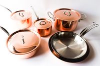 A collection of copper cookware including pots and pans with stainless steel interiors and lids