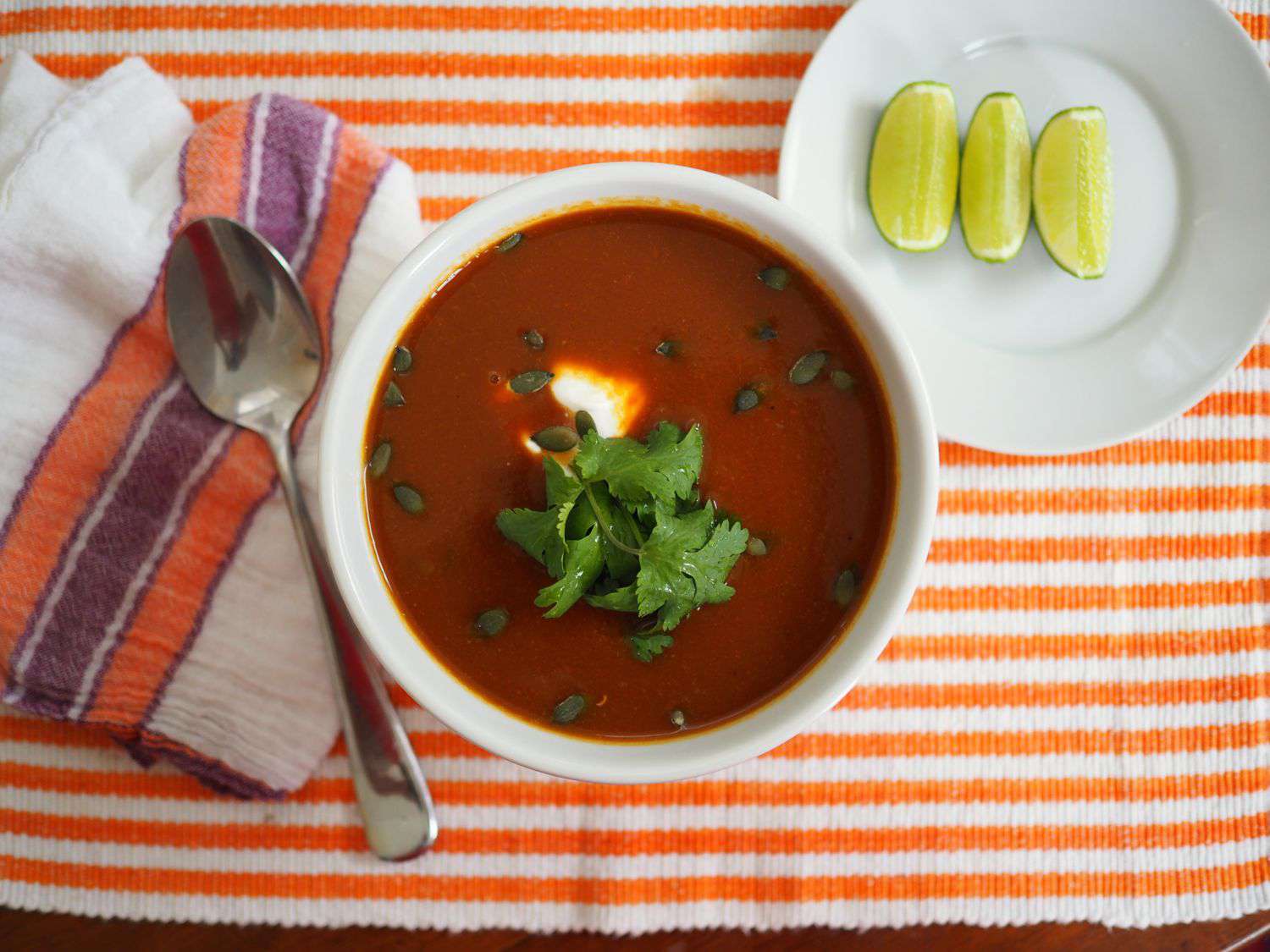 A bowl of butternut squash soup with ancho chile, crema, and pepitas, served with lime wedges..