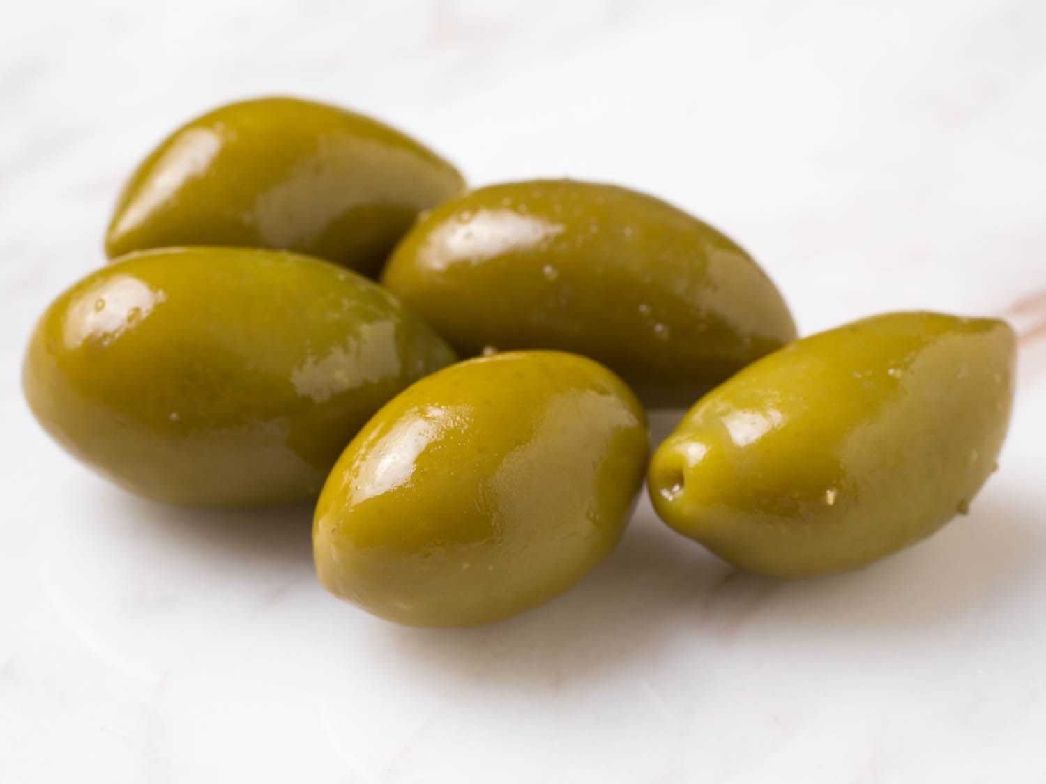 Closeup of cluster of shiny green almond-shaped olives on marble countertop