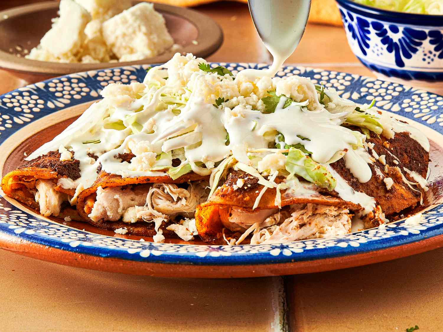 Plate of enchiladas topped with shredded lettuce cheese and crema being drizzled with additional sauce