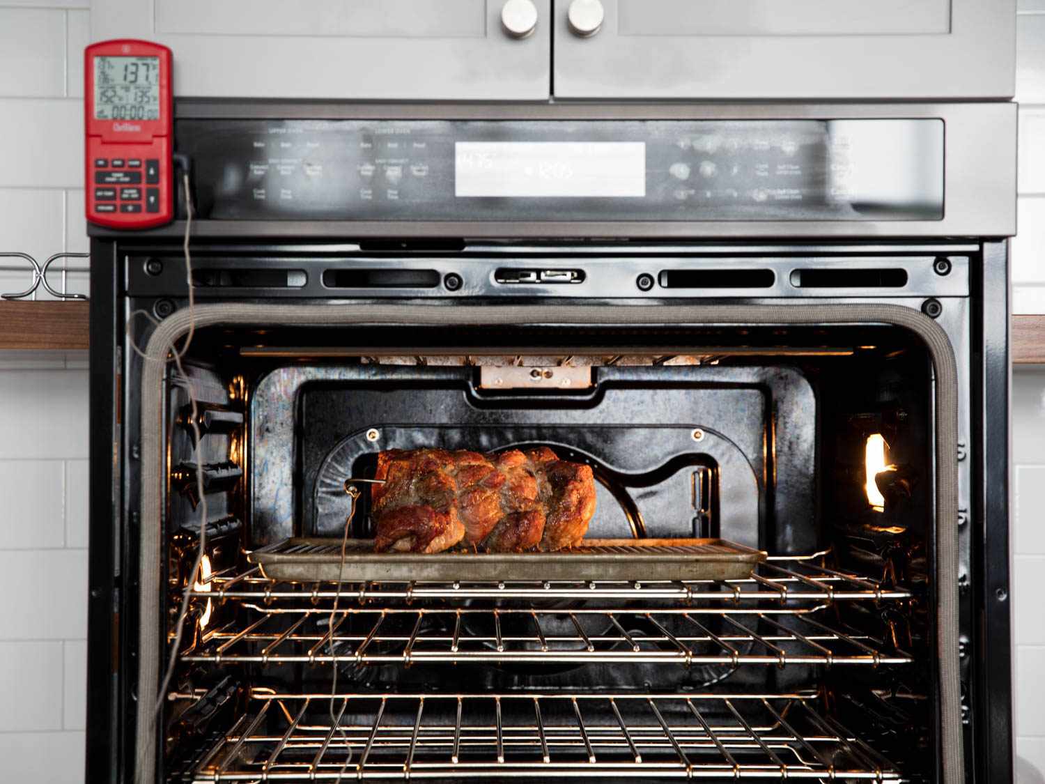 A chicken roasting inside an oven with a probe thermometer panel on the outside of the oven