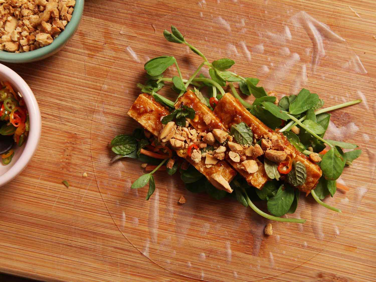 A moistened rice paper wrapper has been set on a work surface and all the spring roll fillings have been arranged in the center.