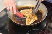 A person checks the temperature of chicken cooking in the Vollrath 12.5 Inch French Style Carbon Steel Fry Pan