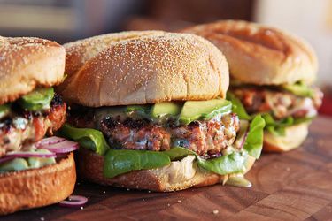 Profile view of Easy Salmon Burgers With Dill Honey-Mustard, Horseradish, and Avocado, assembled on a cutting board.