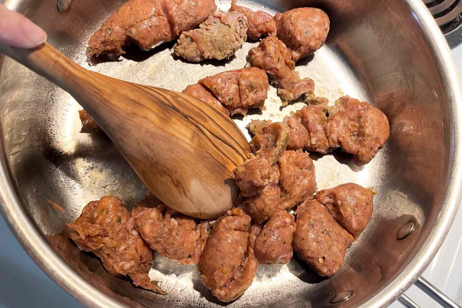 Chunks of sausage being stirred in a skillet with a Sabatier All-Purpose Spoon