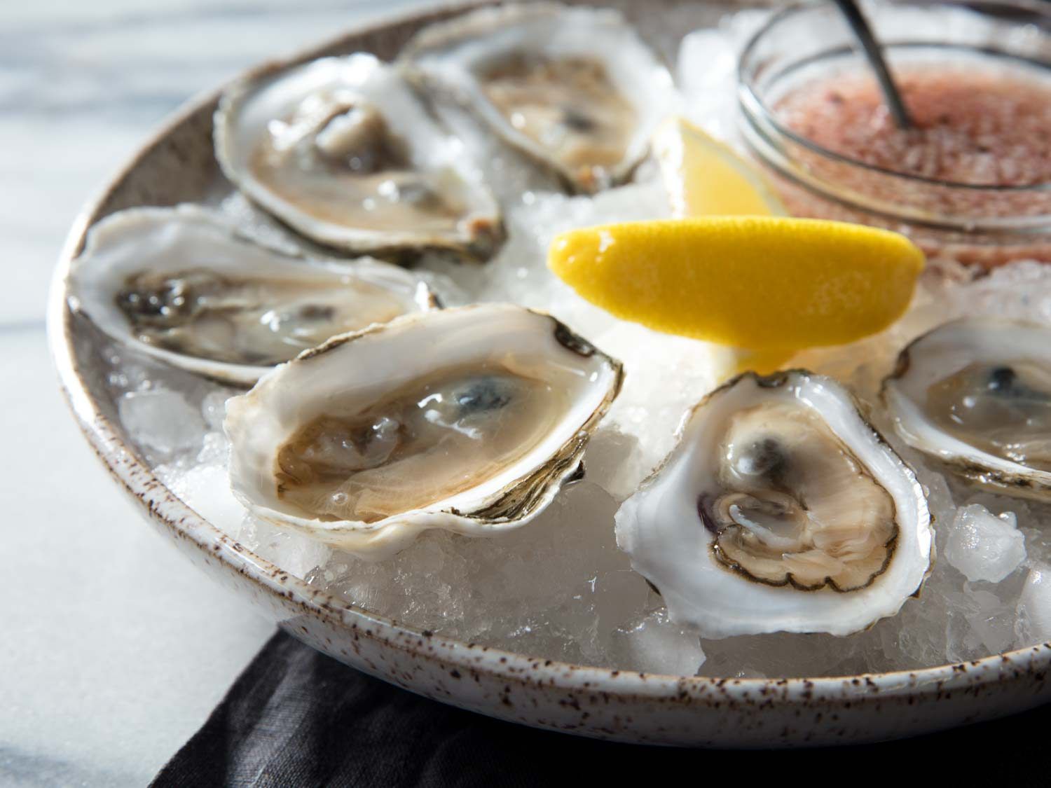 Side view of bowl of oysters with mignonette and lemon wedges