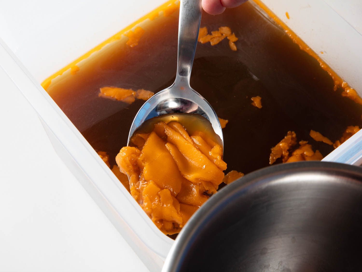 Removing congealed fat from duck stock with a spoon. 