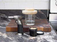 the cocktail topper on a glass with the butane torch and wood chips