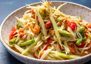 Side view of som tum thai (green papaya salad) in a serving bowl.