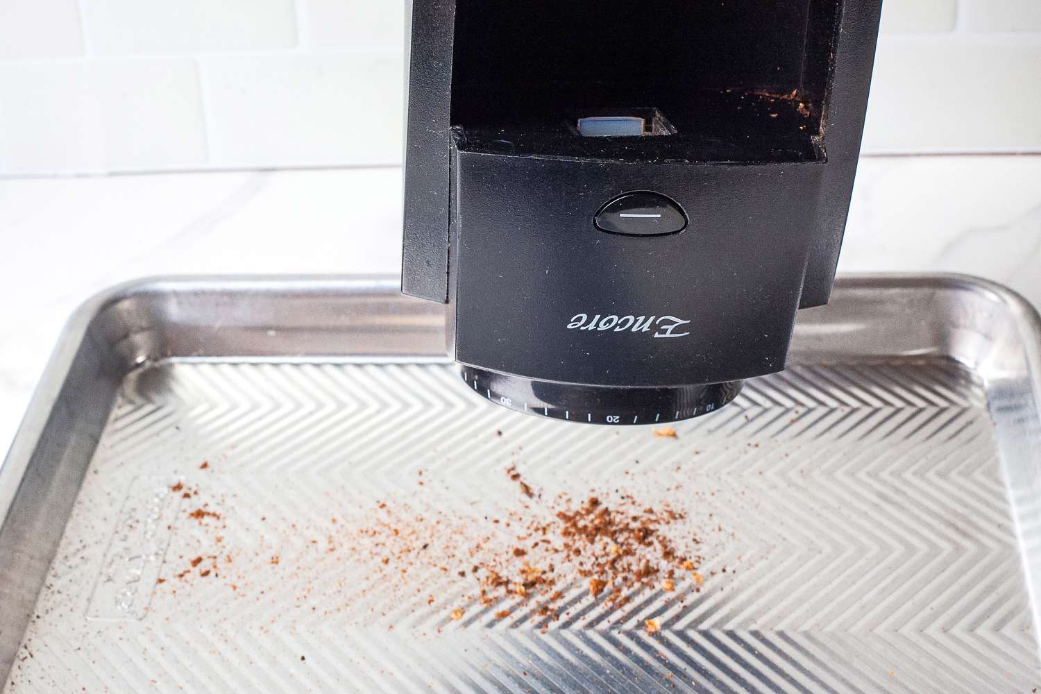 A coffee grinder emptying grounds onto a metal tray below.