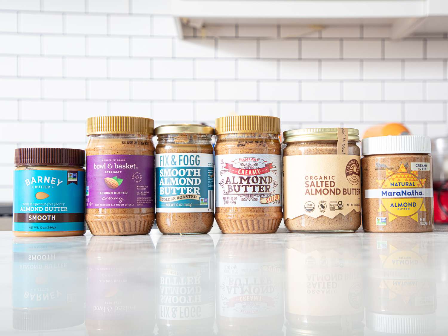 Six almond butter jars arranged on a kitchen counter