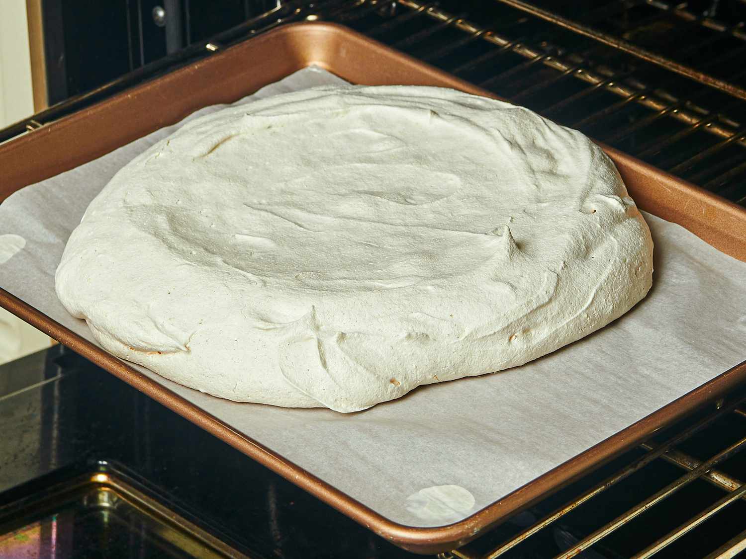 Meringue pavlova base baking in the oven on parchment